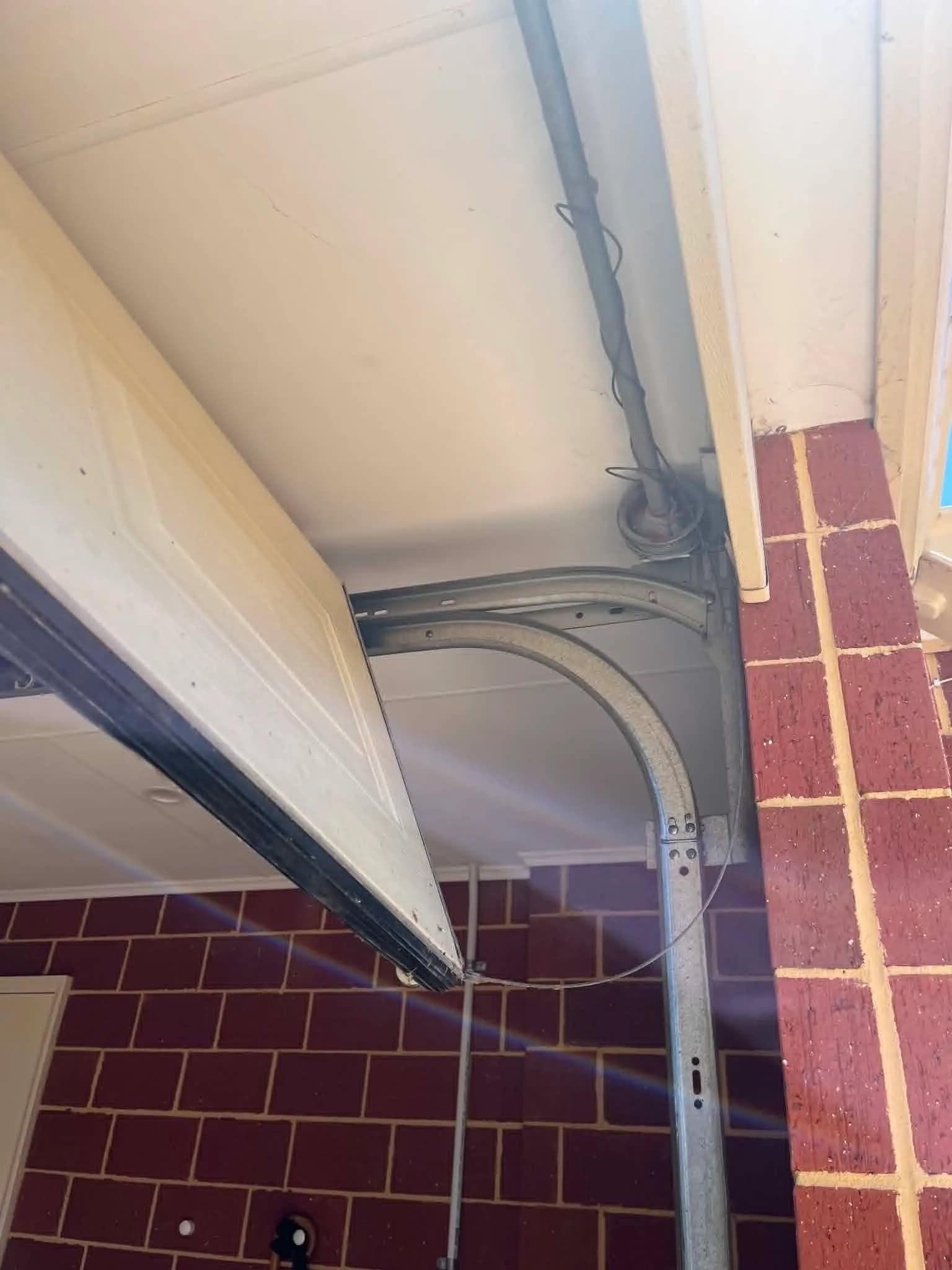 Snapped lift cable hanging beside the curved track of an open sectional garage door