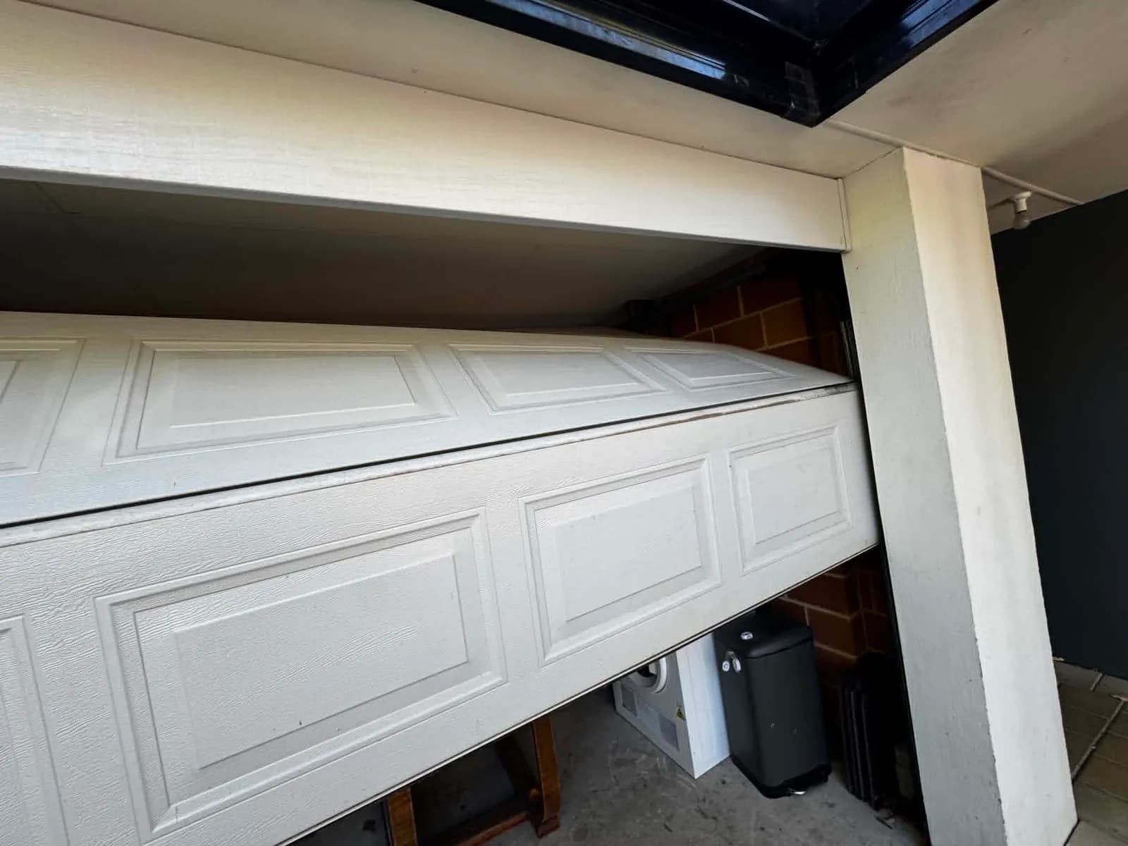 Sectional garage door jammed off its tracks with the top panel dislodged and tilted inside the garage