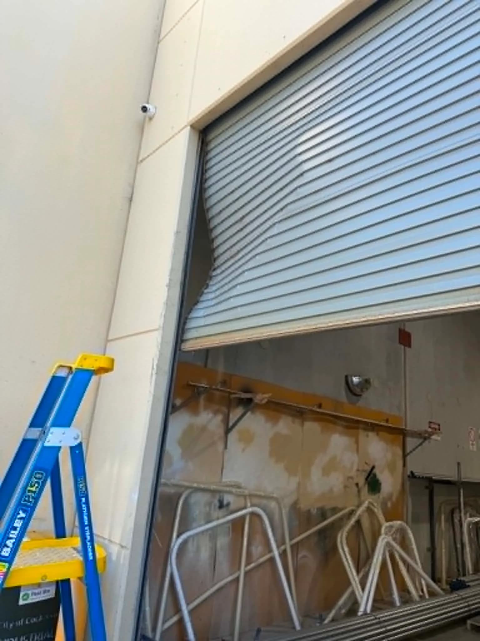Light-blue commercial roller shutter bowed out of its guide above a loading bay in Kewdale Light-blue commercial roller shutter bowed out of its guide above a loading bay in Kewdale