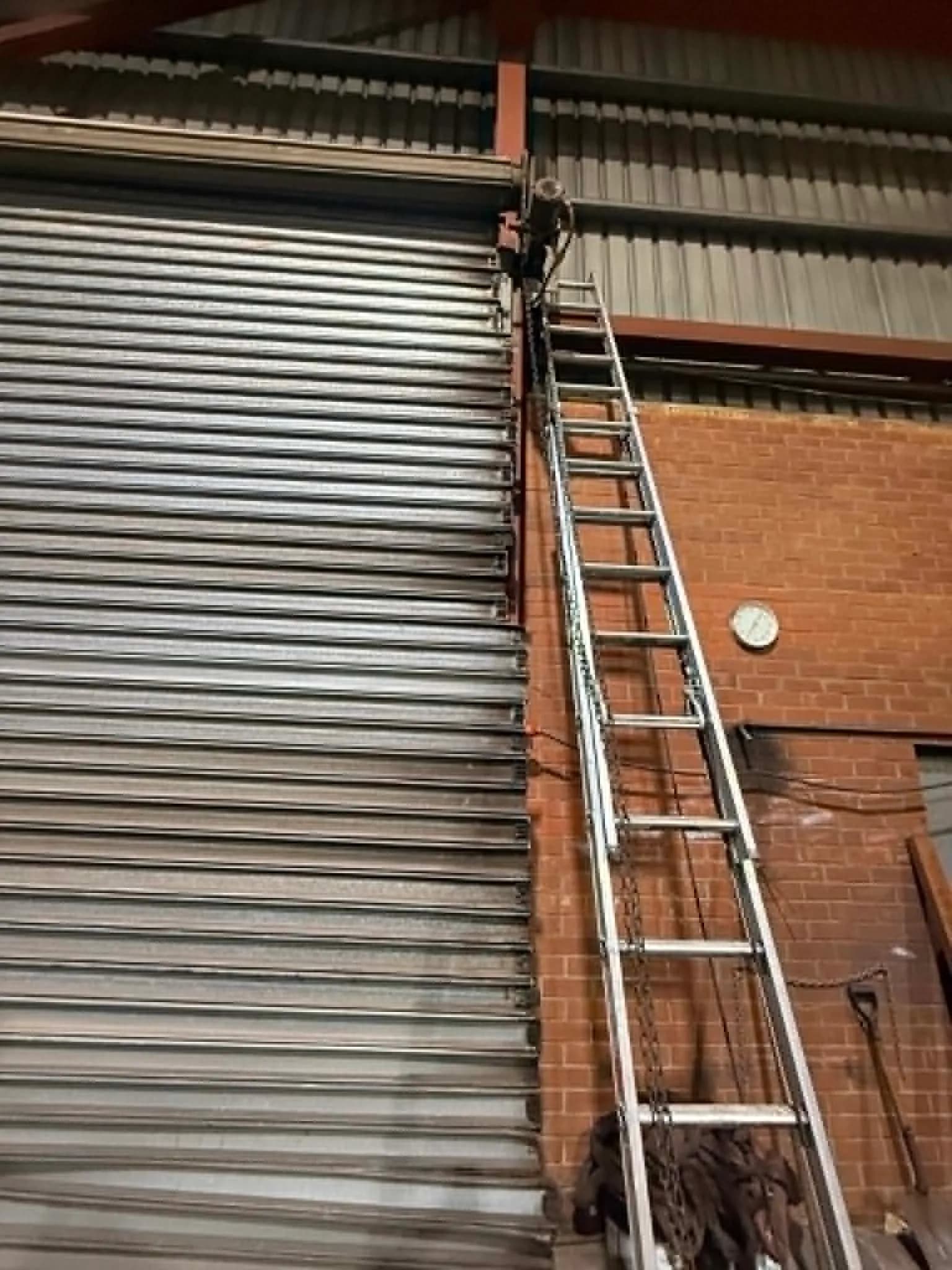 Extension ladder against a large galvanised industrial roller shutter in a Malaga warehouse Extension ladder against a large galvanised industrial roller shutter in a Malaga warehouse