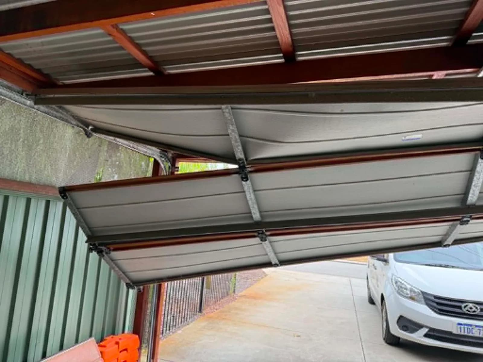 Sectional garage door with buckled panels hanging under a carport in Canning Vale Sectional garage door with buckled panels hanging under a carport in Canning Vale