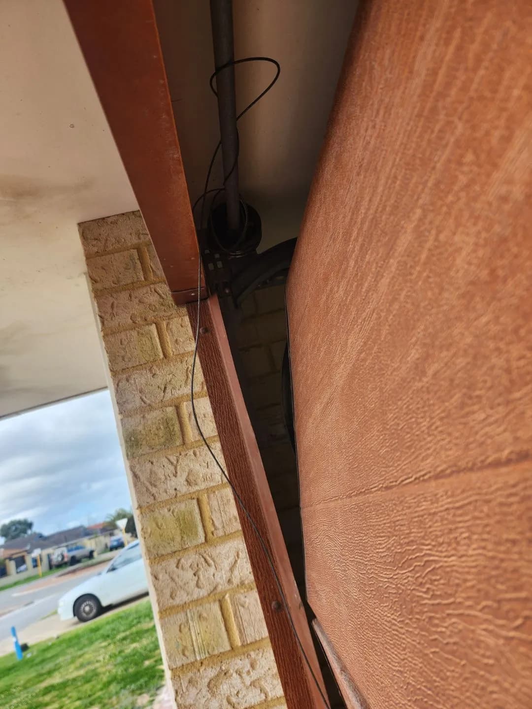 Woodgrain sectional garage door in Bennett Springs, Perth pushed out of its guide with the lift cable hanging slack after a car hit it Woodgrain sectional garage door in Bennett Springs, Perth pushed out of its guide with the lift cable hanging slack after a car hit it