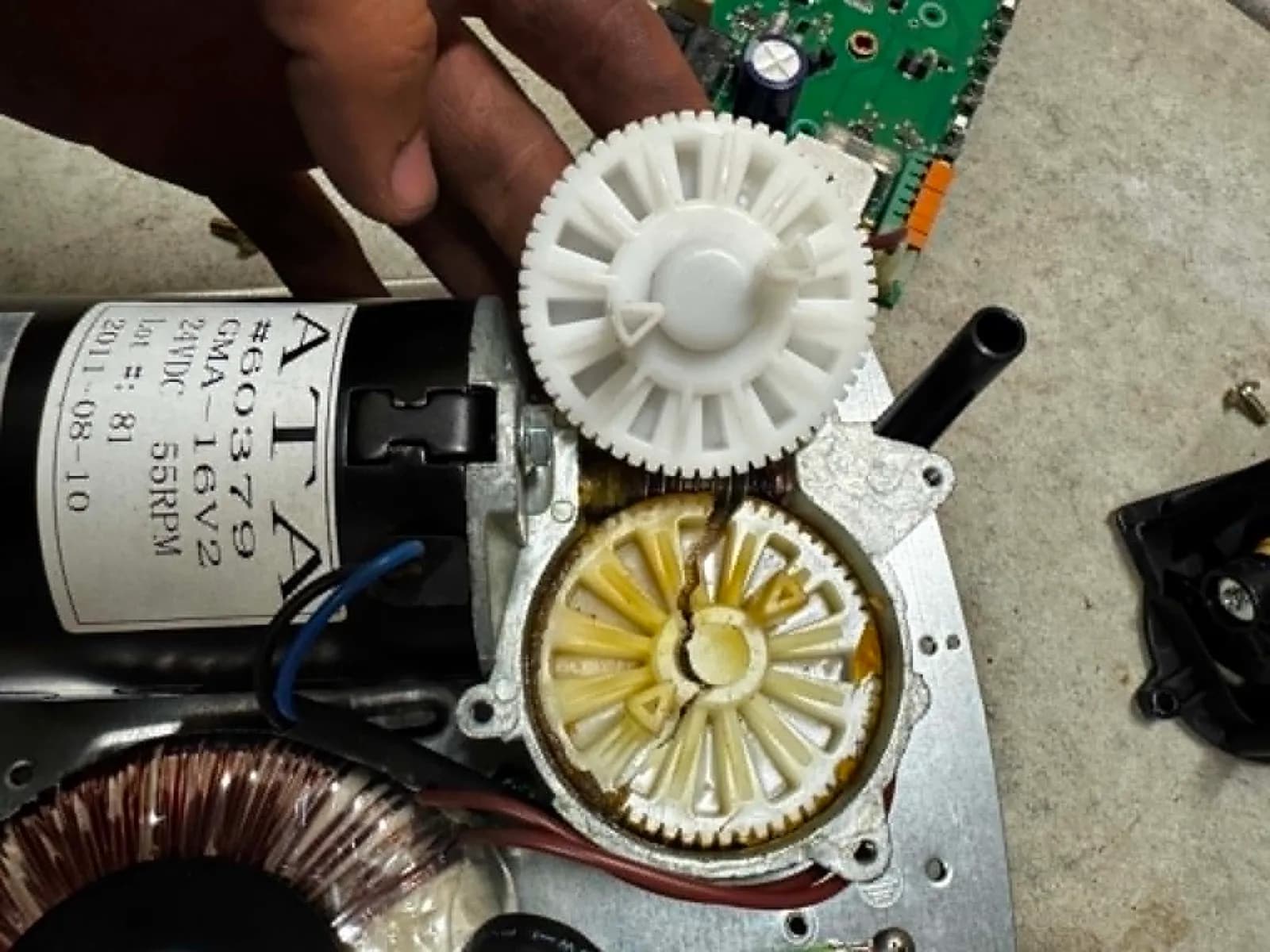 How to Reset a Garage Door Opener & Remote (Step by Step) Technician holding a new nylon drive gear beside the stripped gear inside a garage door motor