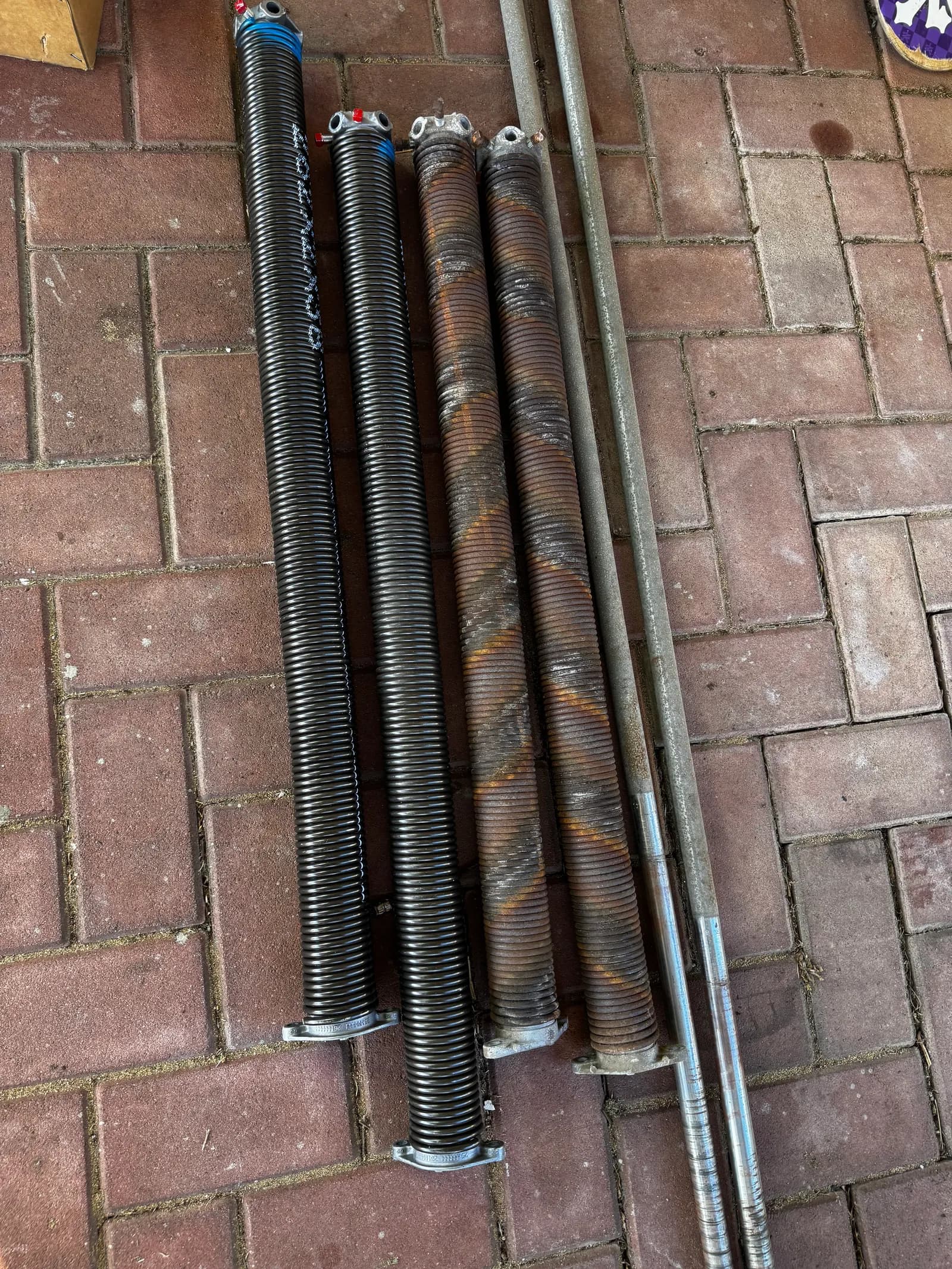 Old rusted springs and shaft laid out next to the new springs and torsion pipe Old rusted springs and shaft laid out next to the new springs and torsion pipe