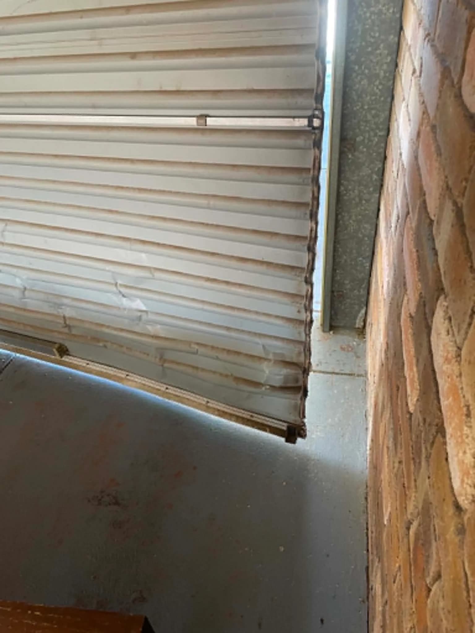 White roller door curtain dislodged from its guide against a brick wall in Wanneroo White roller door curtain dislodged from its guide against a brick wall in Wanneroo