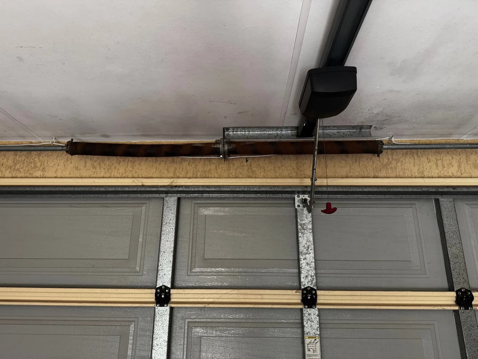 Rusted orange torsion springs above a grey sectional garage door in Caversham, Perth before replacement Rusted orange torsion springs above a grey sectional garage door in Caversham, Perth before replacement