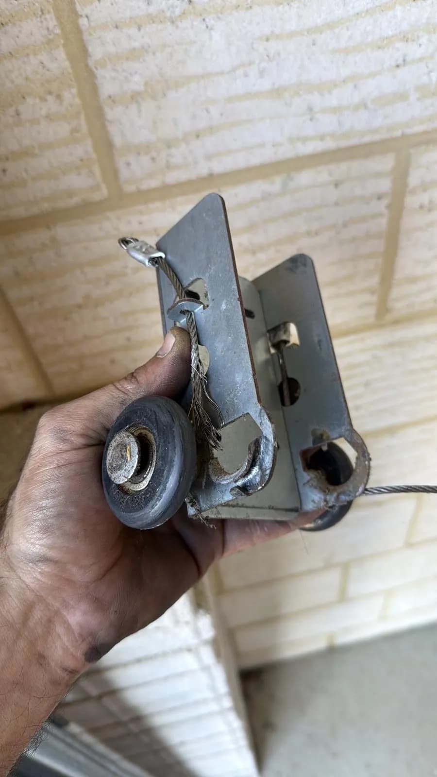 Rusted garage door bottom bracket held in a technician's hand with a frayed, corroded lift cable still attached, removed from a door in Spearwood, Perth Rusted garage door bottom bracket held in a technician's hand with a frayed, corroded lift cable still attached, removed from a door in Spearwood, Perth